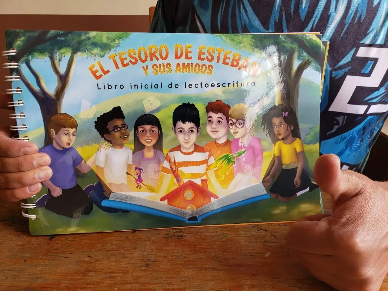 Fotografía real del libro El Tesoro de Esteban y sus Amigos, sostenido sobre una mesa, con encuadernación de espiral